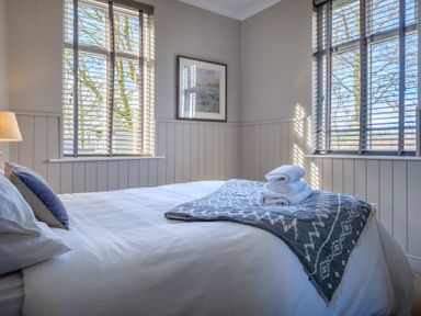A bedroom with a bed, folded towels on a blanket, two windows with blinds, a lamp, and a framed picture on the wall at Gate House in Killington near Sedbergh