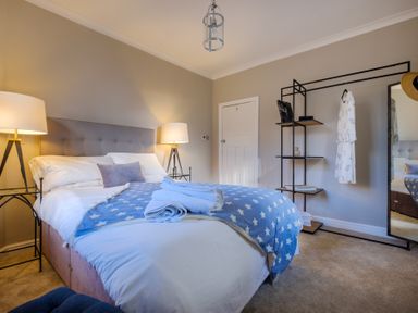 A bedroom with a double bed with blue star blanket two bedside lamps and a black metal clothing rack with mirror at Gate House Killington near Sedbergh