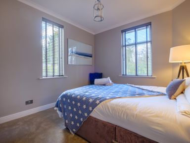 A bedroom with two windows a bed with star patterned blanket a lamp and a chair at Gate House in Killington near Sedbergh