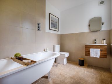 A bathroom with a bathtub a toilet a wooden vanity with a towel and mirror at Gate House Killington near Sedbergh