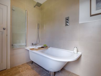 A bathroom with a white bathtub a wooden tray shower controls and a jar on the tub edge at Gate House in Killington near Sedbergh