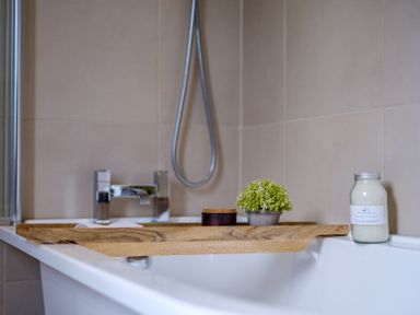A bathtub with a wooden tray holding a small plant and container and bath salts bottle in a bathroom at Gate House in Killington near Sedbergh