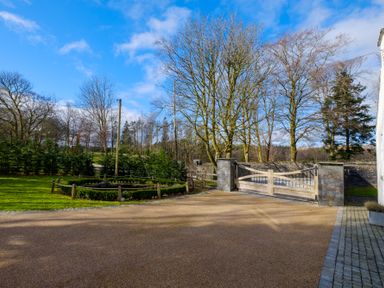 A driveway with a wooden gate and stone pillars with trees and grass surrounding at Gate House Killington near Sedbergh