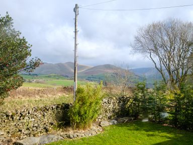 A garden with stone walls a wooden utility pole and trees with hills in the background at Gate House in Killington near Sedbergh