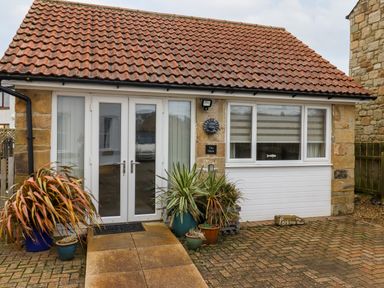 A small stone building with double glass doors and potted plants outside at The Nook in North Sunderland near Seahouses