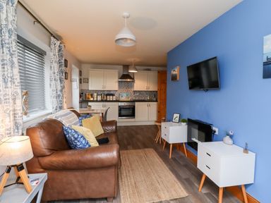 An open living space with a brown leather sofa and white cabinets in a kitchen at The Nook in North Sunderland near Seahouses