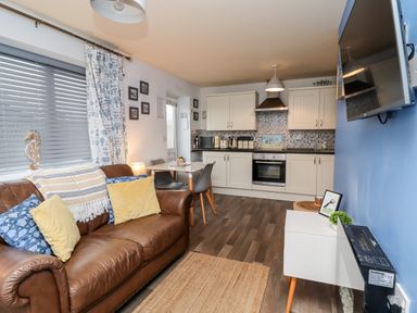 A living area with a brown leather sofa and kitchen with white cabinets and appliances at The Nook in North Sunderland near Seahouses