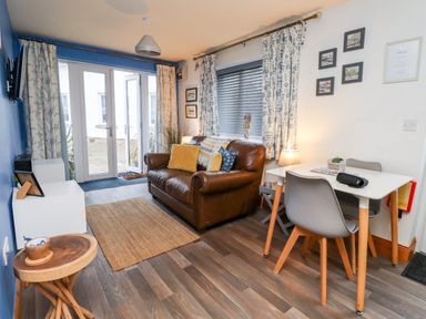 A living room with a brown sofa yellow cushions a small dining table with two chairs and glass doors at The Nook in North Sunderland near Seahouses