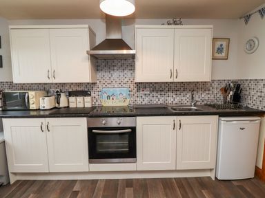 A kitchen with white cabinets a stove a microwave a toaster a kettle containers and a small fridge at The Nook in North Sunderland near Seahouses