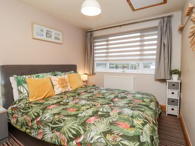 A bedroom with a bed with green tropical patterned bedding and pillows near a window with curtains at The Nook in North Sunderland near Seahouses