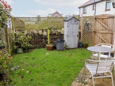 A small garden with grass metal table and chairs wooden shed and potted plants at The Nook in North Sunderland near Seahouses