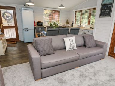A living area with a grey sofa, dining table with chairs, kitchen appliances, and a welcome sign at Tree View Lodge in Troutbeck Bridge