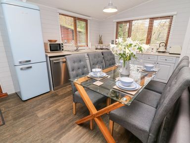 A kitchen with a glass dining table set with dishes and flowers and grey chairs at Tree View Lodge in Troutbeck Bridge