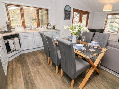 A dining area with a glass table set for six and a kitchen with light cabinets at Tree View Lodge in Troutbeck Bridge