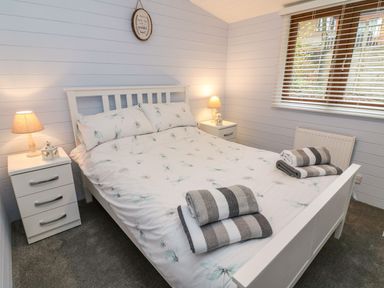 A bedroom with a white bed and floral bedding two bedside tables with lamps and folded towels on the bed at Tree View Lodge in Troutbeck Bridge