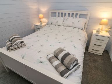 A bedroom with a bed with floral bedding and two rolled towels on it two bedside tables with lamps and decorative items at Tree View Lodge in Troutbeck Bridge