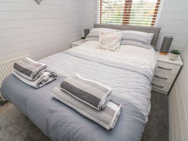 A bedroom with a bed with striped bedding and folded towels on top at Tree View Lodge in Troutbeck Bridge