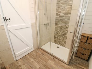 A bathroom with a glass shower enclosure wooden floor a white door and a wicker storage unit at Tree View Lodge in Troutbeck Bridge