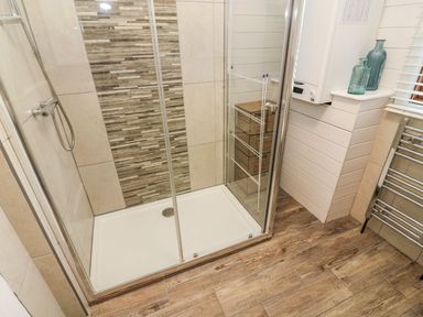 A shower enclosure with glass doors a tiled wall feature and wooden floor at Tree View Lodge in Troutbeck Bridge