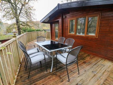 An outdoor wooden deck with a metal table and six mesh chairs at Tree View Lodge in Troutbeck Bridge