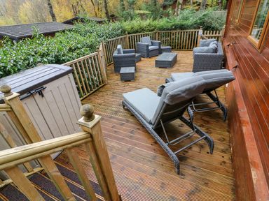 An outdoor wooden deck with patio furniture including lounge chairs armchairs a sofa and a storage shed at Tree View Lodge in Troutbeck Bridge