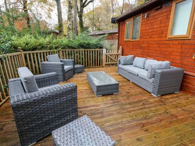An outdoor deck with grey wicker seating and a glass coffee table at Tree View Lodge in Troutbeck Bridge