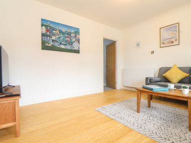 A living room with a wooden coffee table, gray sofa with a yellow cushion, TV on wooden stand, two paintings on the walls and wooden floor at Lakeside in Falmouth