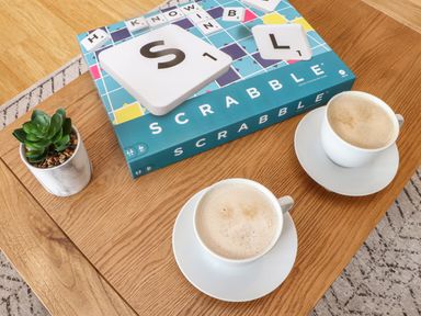 A wooden table with a Scrabble game box two cups of coffee and a small potted plant
