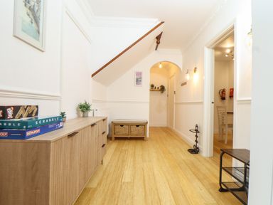 A hallway with wooden cabinets board games and plants under stairs at Lakeside in Falmouth