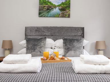 A bed with gray pillows and white towels with orange juice and toast on a tray at Lakeside in Falmouth