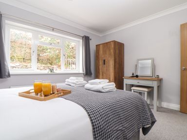 A bedroom with a bed with folded towels and a tray with two glasses of orange juice a wardrobe and a dressing table with a mirror at Lakeside in Falmouth
