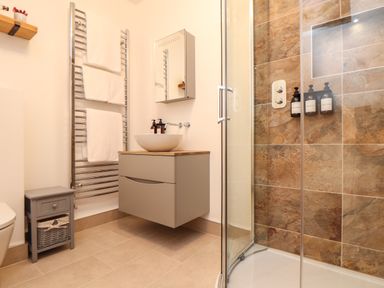 A bathroom with a shower enclosure with brown tiles a floating vanity with a sink mirror cabinet towels on a rack and a small storage unit at Lakeside in Falmouth