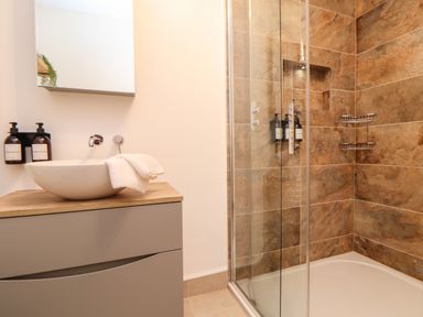 A bathroom with a sink on a wooden vanity and a glass shower enclosure with brown tiles at Lakeside in Falmouth