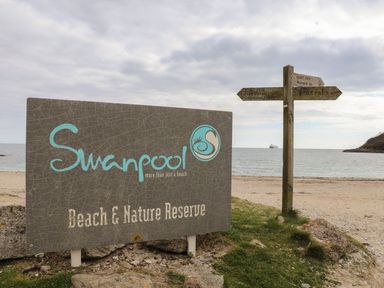A beach with a sign for Swanpool Beach and Nature Reserve and a wooden directional sign near the shore at Lakeside in Falmouth