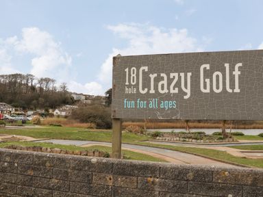 A sign for 18 hole Crazy Golf with a golf course and houses in the background at Lakeside in Falmouth