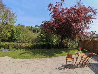 An outdoor patio area with a small wooden table and two chairs next to a lawn and red-leafed tree at Lakeside in Falmouth