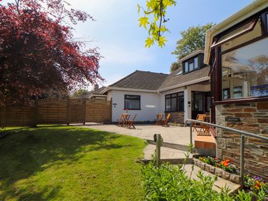 A garden patio with wooden chairs and tables outside a house with white walls and stone detailing at Lakeside in Falmouth