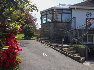 A driveway with the number 4 painted on it leading to a building with stone and glass walls and stairs surrounded by flowers at Lakeside in Falmouth