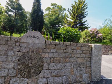A stone wall with a circular stone design and the word Lakeside surrounded by trees and bushes at Lakeside in Falmouth