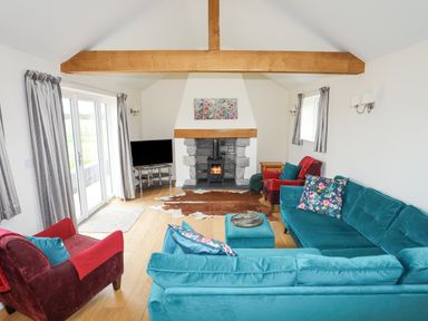 A living room with a blue sofa set a red armchair a fireplace and a television at The Piggery in LLanfair Talhaiarn near Abergele