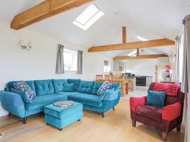 A living room with blue sectional sofa red armchair wooden dining table and exposed wooden beams at The Piggery in LLanfair Talhaiarn near Abergele