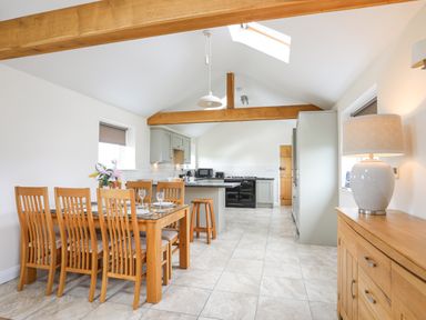 A kitchen and dining area with wooden chairs and table an island and appliances at The Piggery in Llanfair Talhaiarn near Abergele