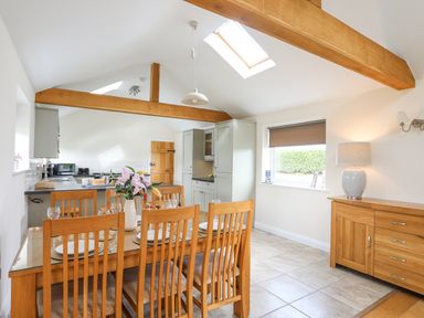 A dining area with wooden table and chairs next to a kitchen with cabinets and skylight at The Piggery in LLanfair Talhaiarn near Abergele