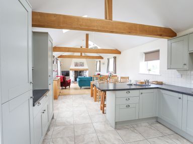 A kitchen with light gray cabinets and black countertops opening to a dining area with a wooden table and chairs at The Piggery in Llanfair Talhaiarn near Abergele