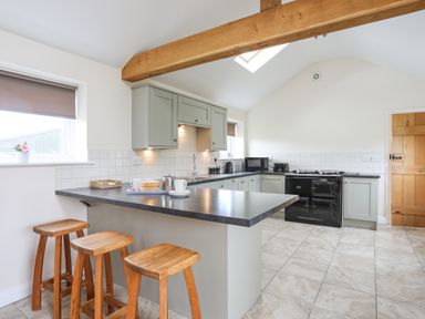 A kitchen with a large countertop island and three wooden stools at The Piggery in LLanfair Talhaiarn near Abergele