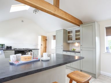 A kitchen with grey cabinets a black stove a wooden beam and a countertop with a cake and cups at The Piggery LLanfair Talhaiarn near Abergele