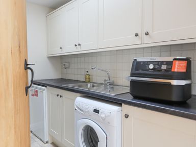 A utility room with washing machine sink countertop and white cabinets at The Piggery in LLanfair Talhaiarn near Abergele