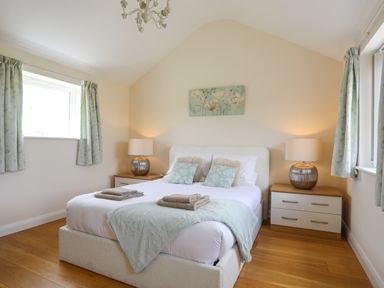 A bedroom with a double bed two bedside tables with lamps and two windows with curtains at The Piggery in LLanfair Talhaiarn near Abergele