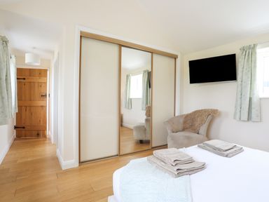 A bedroom with a bed and towels a chair a wall mounted TV and sliding mirrored wardrobe doors at The Piggery in LLanfair Talhaiarn near Abergele