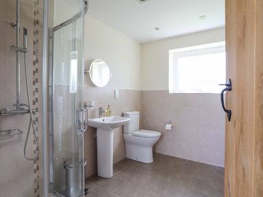 A bathroom with a shower, sink, toilet, round mirror and a window at The Piggery in LLanfair Talhaiarn near Abergele